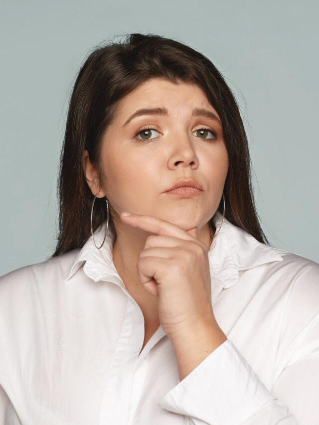 Human facial expressions, feelings and emotions. Studio image of pensive thoughtful young European businesswoman with large curvy body touching her chin, thinking over creative business ideas